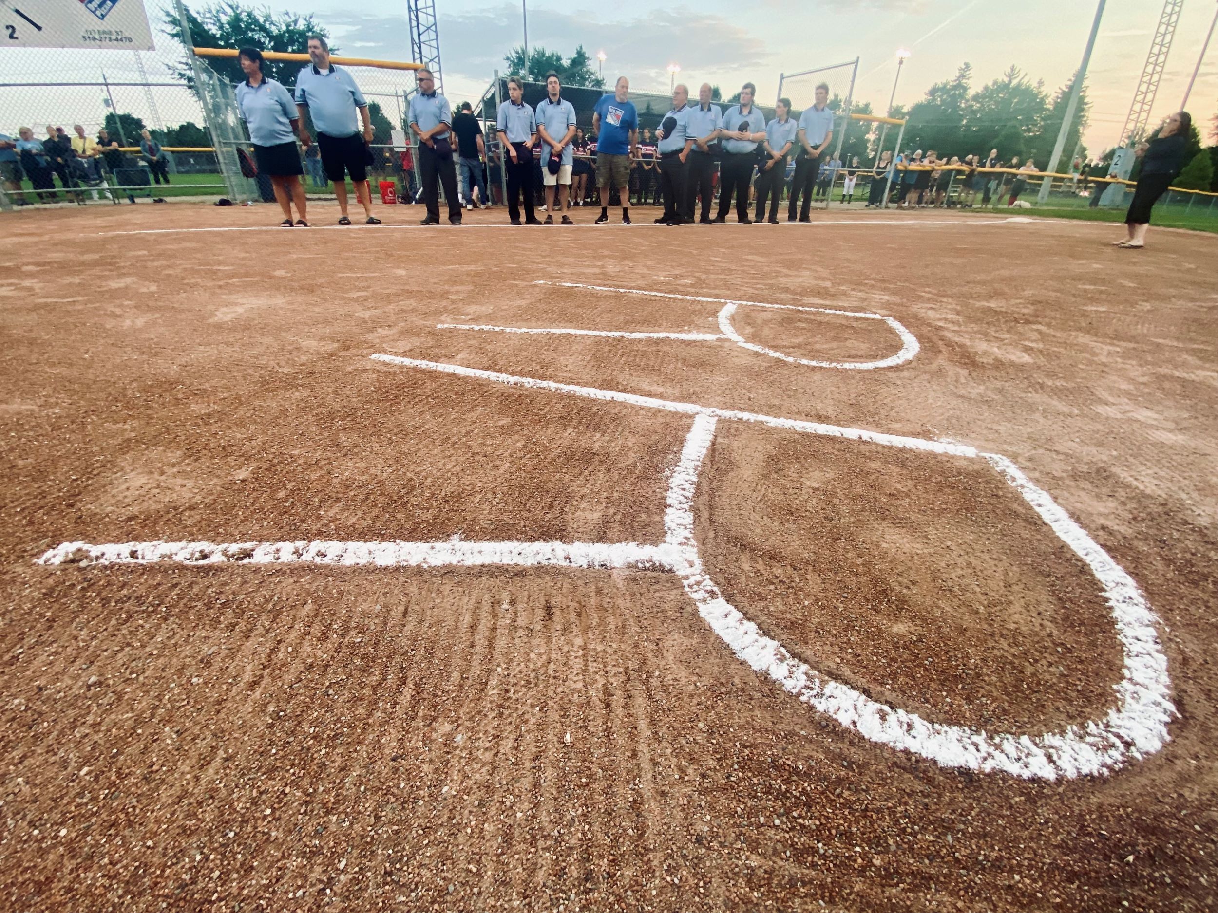 Umpires line the baselines and behind home plate before a girls U17 fastball game between Stratford and London at Anne Hathaway Park in Stratford to pay their respects to Rick Rogers on Tuesday, July 23, 2024. (Cory Smith/Stratford Beacon Herald)