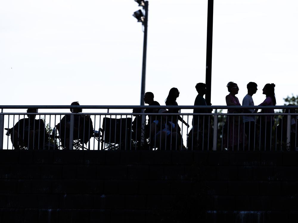 Ticketless fans gather nightly on a riverbank within sight and earshot of the big rock festival, forming a lively and free viewing party.