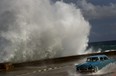 A driver maneuvers his classic American car along a wet road as a wave crashes against the Malecon in Havana, Cuba, Thursday, Oct. 25, 2012. Hurricane Sandy blasted across eastern Cuba on Thursday as a potent Category 2 storm and headed for the Bahamas after causing at least two deaths in the Caribbean. (AP Photo/Ramon Espinosa)