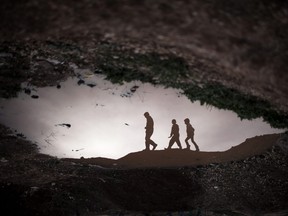 Displaced Syrian children are reflected in a puddle as they walk through an olive tree field near the Azaz camp for displaced people, north of Aleppo province, Syria, Thursday, Feb. 21, 2013. According to Syrian activists the number of people in the Azaz camp has grown by 3,000 in the last weeks due to heavier shelling by government forces. (AP Photo/Manu Brabo)