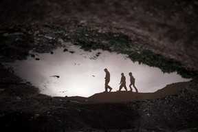 Displaced Syrian children are reflected in a puddle as they walk through an olive tree field near the Azaz camp for displaced people, north of Aleppo province, Syria, Thursday, Feb. 21, 2013. According to Syrian activists the number of people in the Azaz camp has grown by 3,000 in the last weeks due to heavier shelling by government forces. (AP Photo/Manu Brabo)