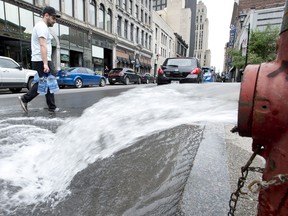 A man crosses a street carrying litres of water as water pours out of a fire hydrant on Wednesday. Montreal has issued a boil-water advisory to a large swath of the city affecting over one million residents after a water-filtration station broke down. THE CANADIAN PRESS/Paul Chiasson