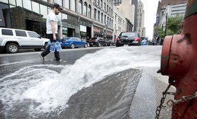 A man crosses a street carrying litres of water as water pours out of a fire hydrant on Wednesday. Montreal has issued a boil-water advisory to a large swath of the city affecting over one million residents after a water-filtration station broke down. THE CANADIAN PRESS/Paul Chiasson