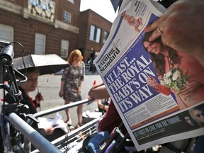 A news cameraman reads a newspaper across St. Mary's Hospital exclusive Lindo Wing in London, Monday, July 22, 2013. Prince William's wife, Kate Middleton, the Duchess of Cambridge, gave birth to an eight pound, six ounce baby boy at 4:24 p.m. London time. The happy news delays if not necessarily dispenses with a possibly divisive debate within the Commonwealth over the rules of royal succession had the third heir to the throne been a girl.  (AP Photo/Lefteris Pitarakis)