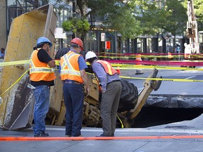 Montreal city workers look at a backhoe that was partly swallowed by a sinkhole earlier today. A broken sewer pipe may be the cause of the city's latest downtown sinkhole, a city official said Monday morning as part of Ste-Catherine St. W., from St-Mathieu St. to Guy St., was completely blocked off by police. The operator of the backhoe was taken to hospital for evaluation.(Marie-France Coallier/ THE GAZETTE)