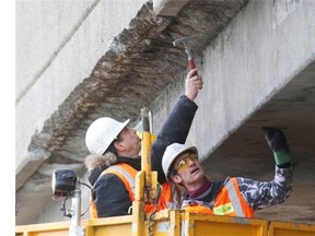 Workers inspect the section of the underside of the eastbound Hymus overpass at Highway 40, where a piece of concrete fell on Monday.