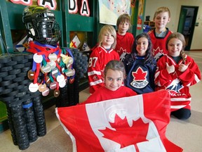 Kindergarten student Nadia Cardillo holds a Canadian flag in front of Grade 5 students, from left, Liam Petraborg, Malcolm Farkas, Naomi Dias, Tristan Koran and Kristina Papoulias, all next to an inukshuk made of hockey pucks.