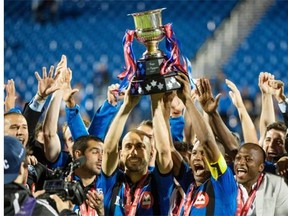 Impact striker Marco Di Vaio, left, and caption Patrice Bernier hois the Voyageurs Cup while surrounded by teammates after beating the Toronto FC 1-0 Wednesday at Saputo Stadium.