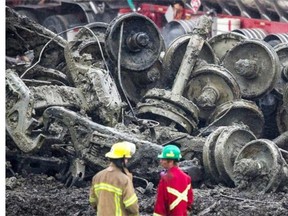Two emergency crew workers speak as they stand in front of a pile of train wheel-set axels inside the red-zone at the site of the explosion in Lac-Mégantic. Around 100 residents were told it will likely take about a year for them be able to live in their homes again.