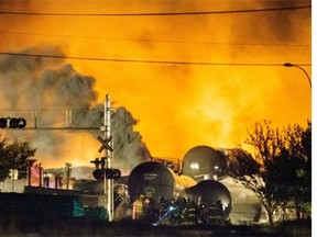 Smoke and fire rises over train cars as firefighters inspect the area after a train carrying crude oil derailed and exploded in the town of Lac-Megantic, 100 kilometres east of Sherbrooke, on Saturday, July 6, 2013.