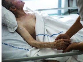 A nurse holds the hand of an elderly patient at a palliative care unit in France.