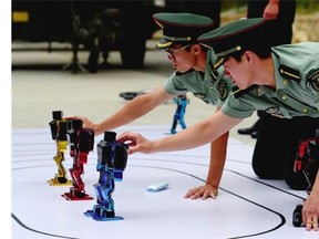 Chinese People's Liberation Army cadets adjust dancing humanoid robots at the PLA's Armoured Forces Engineering Academy in Beijing on July 22, 2014. China's military opened up its engineering academy to journalists on July 22, with demonstrations of rolling tanks, bayonet drills and dancing robots.