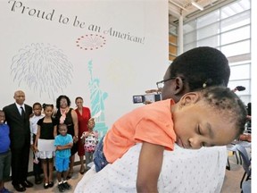 Dammy Oladapo, 3, is held by her father Tosin Oladapo as he makes a photo of his wife, family and friends in front of mural after a naturalization ceremony in Irving, Texas, Thursday, July 3, 2014. The Immigration and Naturalization Service is swearing in over 9,000 new citizens over the Fourth of July holiday week in ceremonies held around the country.