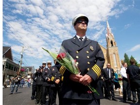 A firefighter from Maine stands with colleagues outside the Ste-Agnès church in Lc-Mégantic, Sunday, July , 2014, during a mass to mark the first anniversary of the trian disaster in that town.  The mass was done as part of weekend activities to commemorate the tragedy.