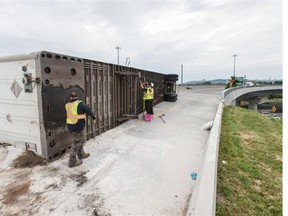 Tow operators work on the overturned container from an large truck that flipped on the Highway 15 northbound ramp from Highway 40 east in Montreal on Monday, July 7, 2014. The truck, which was carrying car axels parts, flipped at around 2:15 a.m.