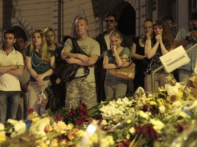 People stand near flower tributes placed outside the Dutch embassy to commemorate victims of Malaysia Airlines plane crash in Kiev, Ukraine, Thursday, July 17, 2014.  A Malaysian Airlines passenger jet was shot down in eastern Ukraine on Thursday, and both the Ukrainian government and pro-Russian rebels blamed one another for the attack. (AP Photo/Sergei Chuzavkov)