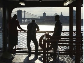 With the Brooklyn Bridge in the background, commuters on the Staten Island Ferry watch the morning sunrise in the New York Harbor in lower Manhattan, July 11, 2014.