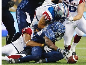 Bombers’ Nic Grigsby reaches for his fumbled ball after being grabbed by Alouettes’ John Bowman (7) and Alan-Michael Cash (91) during the first half in Winnipeg Friday night.