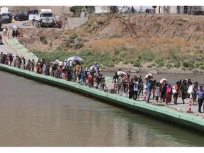 Displaced Iraqis from the Yazidi community cross the Iraqi-Syrian border along the Fishkhabur bridge over Tigris River at the Fishkhabur crossing, in northern Iraq, on August 11, 2014. At least 20,000 civilians, many of whom are from the Yazidi community, who had been besieged by jihadists on a mountain in northern Iraq have safely escaped to Syria and been escorted by Kurdish forces back into Iraq, officials said. The breakthrough coincided with U.S. air raids on Islamic State fighters in the Sinjar area of northwestern Iraq on August 9, and Kurdish forces from Iraq, Syria and Turkey working together to break the siege of Mount Sinjar and rescue the displaced.