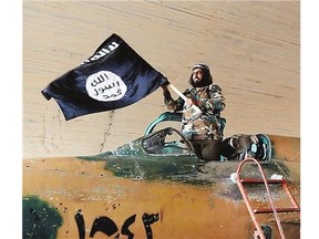 A fighter of the Islamic State group waves a flag from inside a captured government fighter jet following the battle for the Tabqa airbase, in Raqqa, Syria on Sunday.