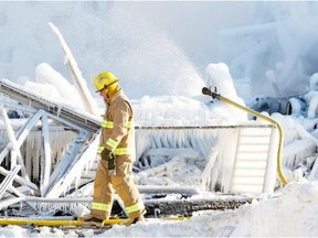 Firefighter walks past hose pouring water on the smouldering remains of a seniors residence in L’Isle-Verte.