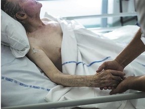 A nurse holds the hand of an elderly patient at a palliative care unit in France.