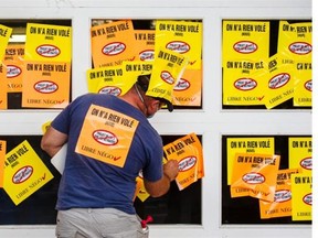 A protester supporting the firefighter’s union places stickers on the garage door entrance to the Montreal City Hall building in protest of the proposed Bill 3, a pension reform bill, in Montreal on Monday, August 18, 2014.