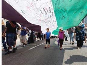 Two young girls walk under a 100 meter long Palestinian flag as they join a march to protest the living conditions in Gaza and the ongoing conflict with Israel. The group marched throughout the streets of Montreal on Sunday Aug. 10, 2014.