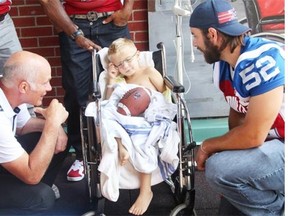 Alouettes head coach Tom Higgins, left, and team player Nicolas Boulay, right, smile as Montreal Children Hospital’s patient 4-year-old Anthony Blais-Lamoureux closes his eyes, not comfortable with all the media attention. Alouettes players were visiting sick kids on Tuesday afternoon as they do annually in three different children hospitals in Montreal.