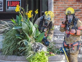 Firefighters remove their masks near a burned propane tank at the scene of an explosion at a residential building on the corner of Bélanger and Fabre Sts. in Montreal on Sunday, September 28, 2014.