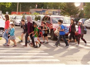 Parents walk their children to school as a traffic guard holds back early morning traffic coming out of the drop off zone in front of Ecole Sainte-Geneviève Ouest in Pierrefonds Thursday, August 28, 2014.