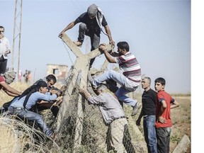 Turkish and Syrian Kurds try to tear down the border fence to cross into neighbouring Syria during a demonstration near the Mursitpinar border crossing at Suruc in Sanliurfa province, on September 26, 2014. Tens of thousands of Syrian Kurds flooded into Turkey fleeing an onslaught by the jihadist Islamic State (IS) group that prompted an appeal for international intervention. Some of the refugee now want to return to protect their homes and join the fight against IS militants.