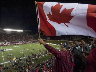 A fan waves a Canadian flag over the Ottawa Redblacks field in a pre-game ceremony in tribute to the two fallen Canadian Armed Forces members, Warrant Officer Patrice Vincent and Cpl. Nathan Cirillo, before a CFL game in Ottawa on Friday, Oct. 24, 2014.