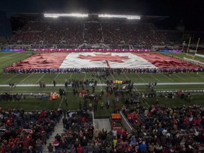 A large Canada flag is unfurled over the Ottawa Redblacks field in a pre-game ceremony in tribute to the two fallen Canadian Armed Forces members, Warrant Officer Patrice Vincent and Cpl. Nathan Cirillo, on Friday, Oct. 24, 2014.