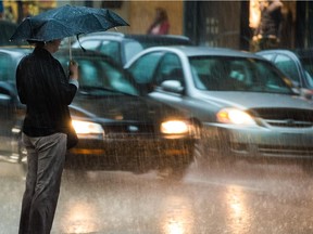 A pedestrian waits to cross Ste. Catherine St. on the corner of Peel St. during a rainstorm in July 2014.