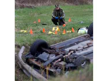 Sûreté du Québec police investigators go over the wreckage of a dead suspect's car after a police shooting in Saint-Jean-sur-Richelieu near Montreal on Monday October 20, 2014.  A motorist ran over 2 pedestrians and fled the scene. He is alleged to have emerged from his vehicle holding a knife after flipping his car.
