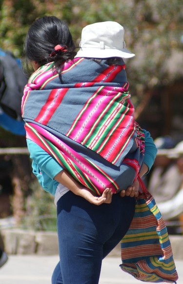 A young woman in Peru carries her child with her while heading to buy vegetables in the fabled Machu Picchu.