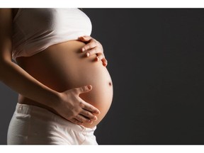 Pregnant woman caressing her belly over gray background