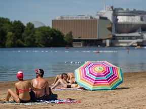 A couple applies sunscreen with the Montreal Casino in the background at the beach at Jean-Drapeau Park in Montreal.