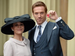 British actor Damian Lewis poses with his wife, Helen McCrory, as he holds his Officer of the Order of the British Empire medal after an investiture ceremony at Buckingham Palace in London on November 26, 2014.