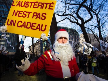 A man in Santa outfit holds a sign as he takes part in an anti-austerity protest in downtown Montreal on Saturday, November 29, 2014.