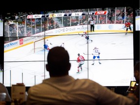 A man in silhouette looks at a TV screen showing a Canadiens-Blackhawks game
