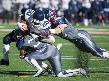 Toronto Argonauts' Steve Slaton (20) is tackled by Montreal Alouettes' Brian Brikowski, right, and Mitchell White during first half CFL football action in Montreal, Sunday, November 2, 2014.