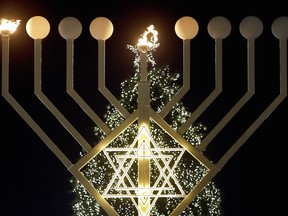 The first flames of a giant Hanukkah Menorah in front of a Christmas tree at the Brandenburg Gate in Berlin, Germany, Tuesday, Dec. 16, 2014 burn at the launch of the eight-day Jewish Festival of Lights.
