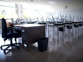An empty teacher's desk is at the front of an empty classroom.