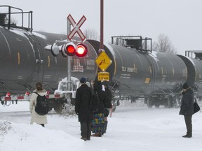 Passengers wait for a freight train to pass before crossing the tracks to catch the AMT commuter train, at the AMT station in Baie d'Urfé, December 2014.