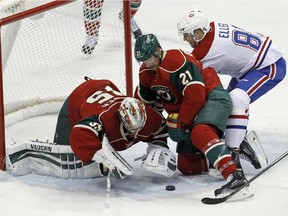 Minnesota Wild goalie Darcy Kuemper, left, dives on the puck under Wild centre Kyle Brodziak (21) and Montreal Canadiens centre Lars Eller, right, of Denmark, during the third period of an NHL hockey game in St. Paul, Minn., Wednesday, Dec. 3, 2014. The Wild won 2-1.