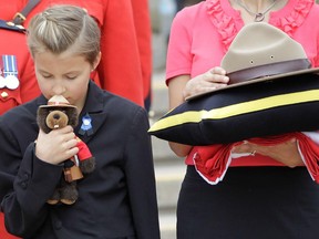 MONCTON, N.B.: June 10, 2014 -- Cst. Fabrice Gevaudan's step-daughter Emma holds a doll as his widow, Angela, holds his hat as they stand outside the Moncton Coliseum after the R.C.M.P. regimental funeral in Moncton, New Brunswick Tuesday, June 10, 2014 for three R.C.M.P. officers.  Cst. Fabrice Georges Gevaudan, Cst. Dave Joseph Ross, and Cst. Douglas James Larche were killed by a gunman last week. (John Kenney / THE GAZETTE)
WORDS FROM JOHN KENNEY:  The tragedy that befell Moncton, New Brunswick in June, the sudden, brutal killing of 3 young R.C.M.P. officers, would be felt keenly anywhere no matter the size of the community. But that the shootings happened in a small city where many of its citizens had a strong bond with the force, reminders of the tragic event were everywhere; from the signs of support outside homes and businesses to the unbelieving looks of sadness and shock on the faces of much of the populace. There was no doubting the pain in Moncton and the area, but the intensity of the feeling of loss was given even deeper meaning upon witnessing the families  of the killed officers waiting for the corteges bearing the caskets of their loved ones to pass by. Here, Cst. Fabrice Gevaudan's stepdaughter Emma holds a doll as his widow, Angela, holds his hat while solemnly waiting outside the Moncton Coliseum after the R.C.M.P. regimental funeral.