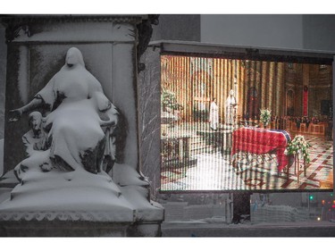 A giant screen shows a live feed of the ceremony for the funeral for Montreal Canadiens great Jean Béliveau as snow covers a religious monument at the Mary Queen of the World Cathedral, where the funeral was held in Montreal on Wednesday, December 10, 2014.