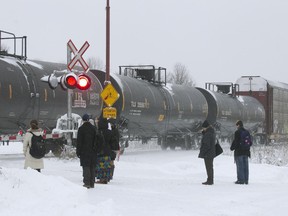 Passengers wait for a freight train to pass before crossing the tracks to catch the AMT communter train, at the AMT station in Baie d'Urfé, Montreal, Thursday December 11, 2014.